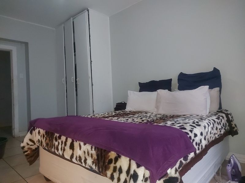 A bedroom featuring tiled flooring and a built-in wardrobe with visible wear and tear on the frame.