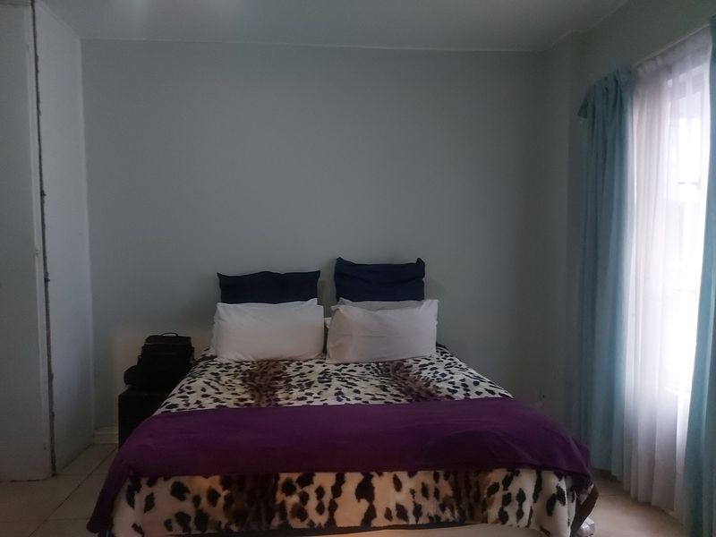 A bedroom featuring tiled flooring and window treatments, currently showing signs of unfinished wall work in the corner.