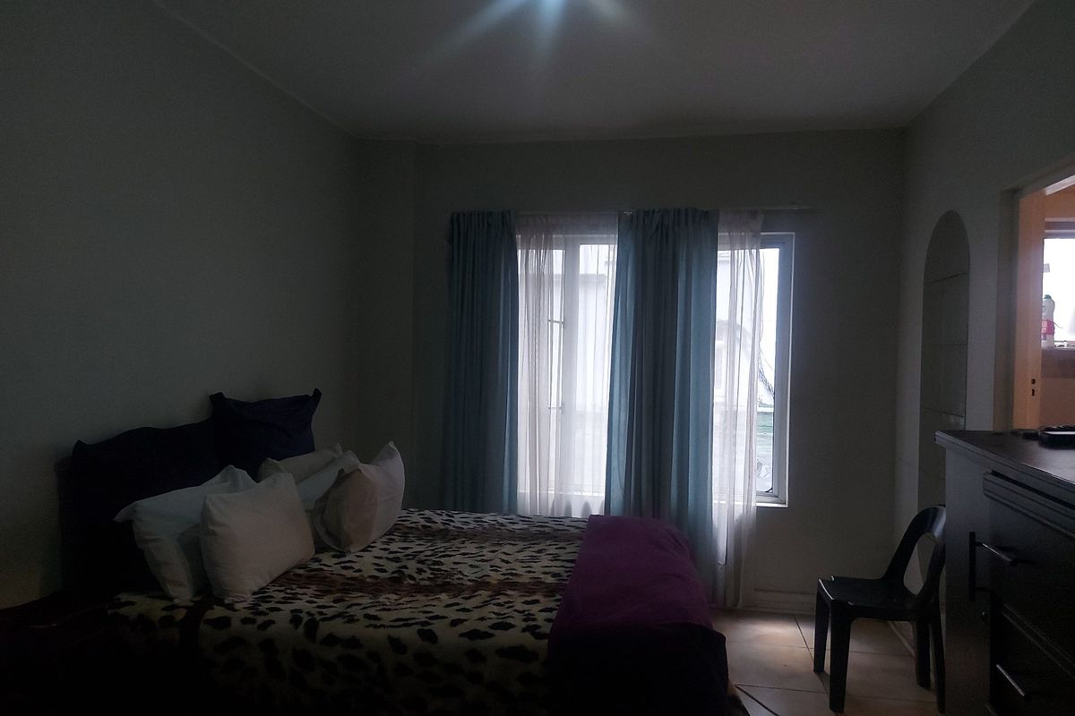 A bedroom featuring tiled flooring and a window with curtains, providing natural light to the space.