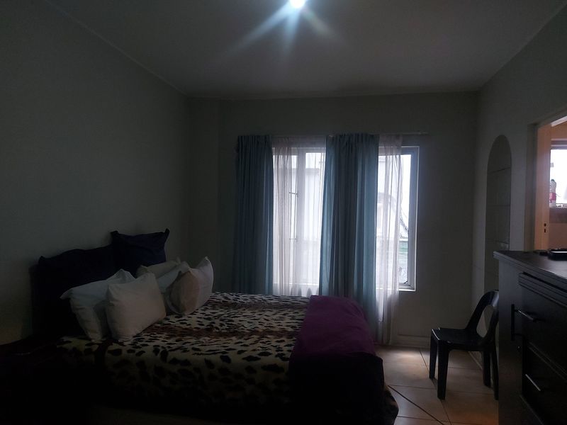 A bedroom featuring tiled flooring and a window with curtains, providing natural light to the space.