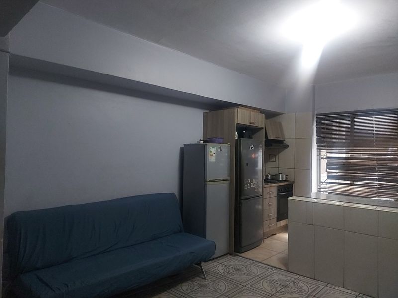 Open plan living and kitchen area featuring tiled flooring, built-in cabinetry, and integrated cooking appliances, offering a functional layout for modern apartment living.