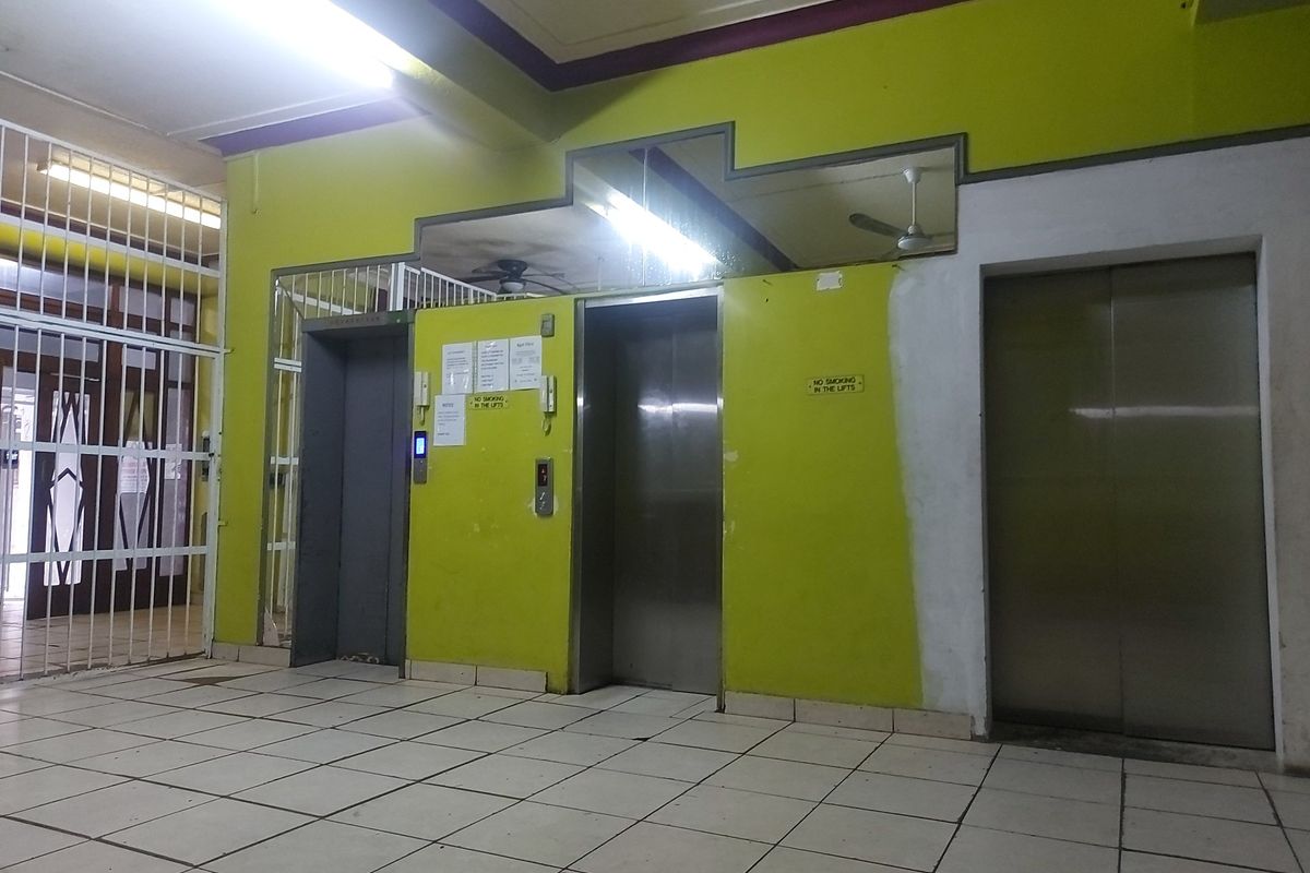 Apartment building lobby area featuring multiple elevators, security gate access, and tiled flooring, currently showing signs of wear and maintenance needs.