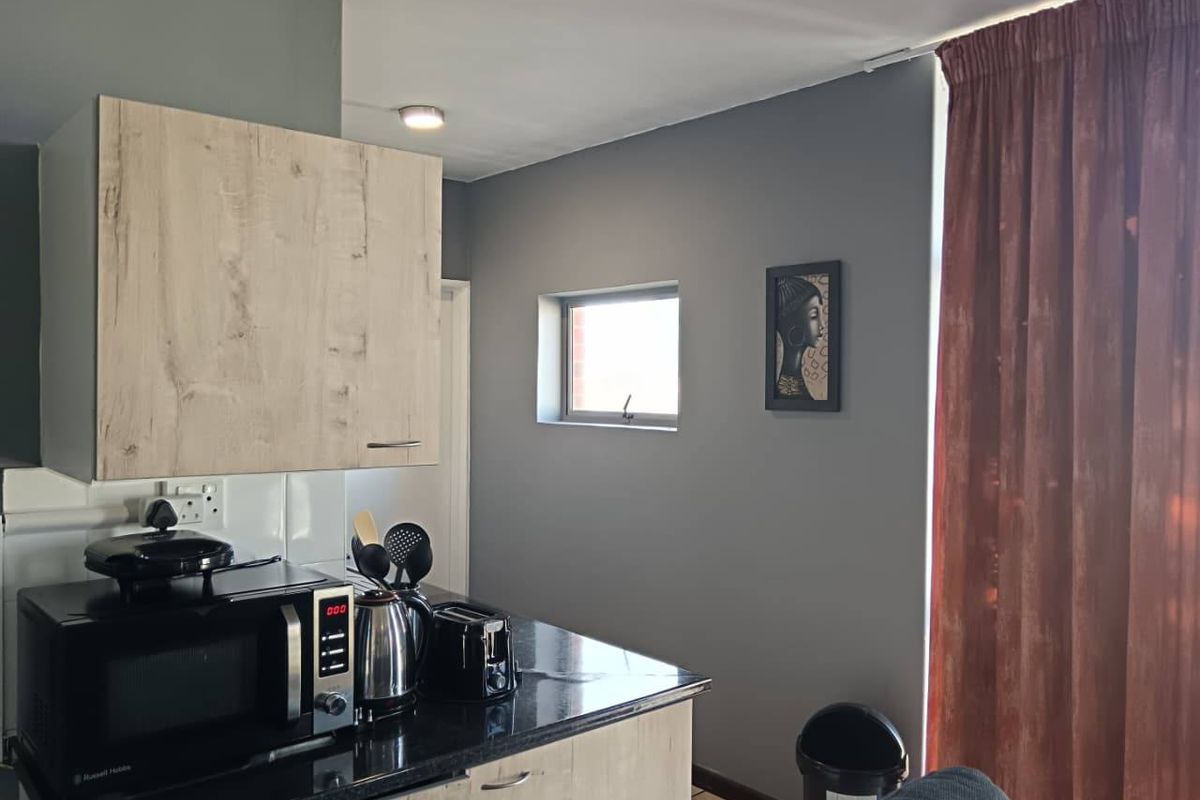 A compact kitchen area featuring light wood-look cabinetry, dark granite countertops, and a tiled backsplash, illuminated by a recessed ceiling light.