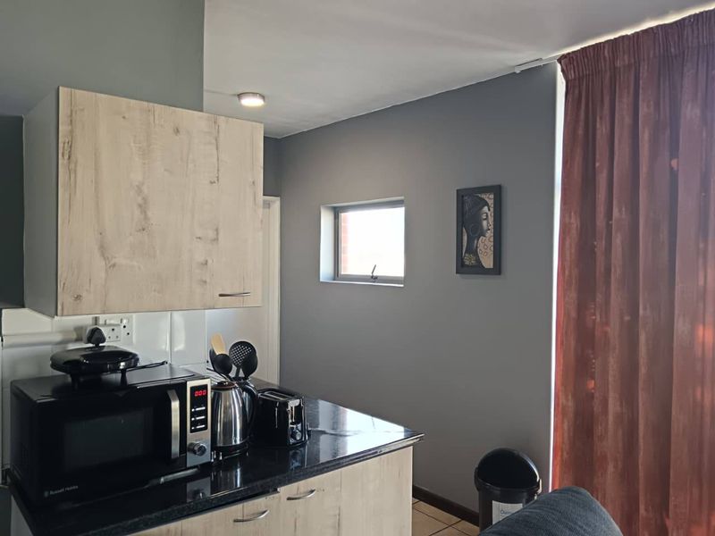 A compact kitchen area featuring light wood-look cabinetry, dark granite countertops, and a tiled backsplash, illuminated by a recessed ceiling light.