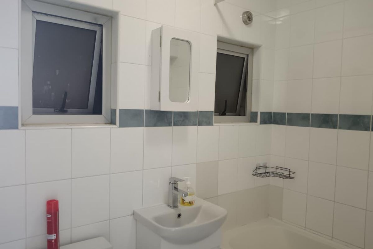 A functional bathroom featuring tiled walls, a vanity basin, a bathtub, and dual casement windows for natural light and ventilation.