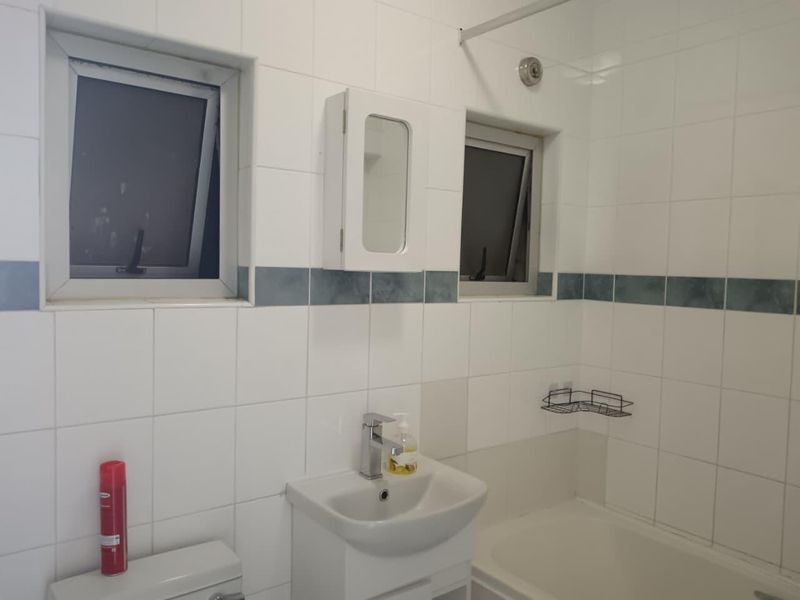 A functional bathroom featuring tiled walls, a vanity basin, a bathtub, and dual casement windows for natural light and ventilation.