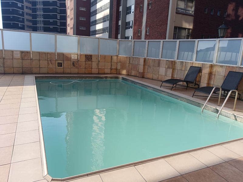 A communal swimming pool area featuring stone-clad walls, glass safety fencing, and a tiled deck, providing a functional outdoor space for residents.