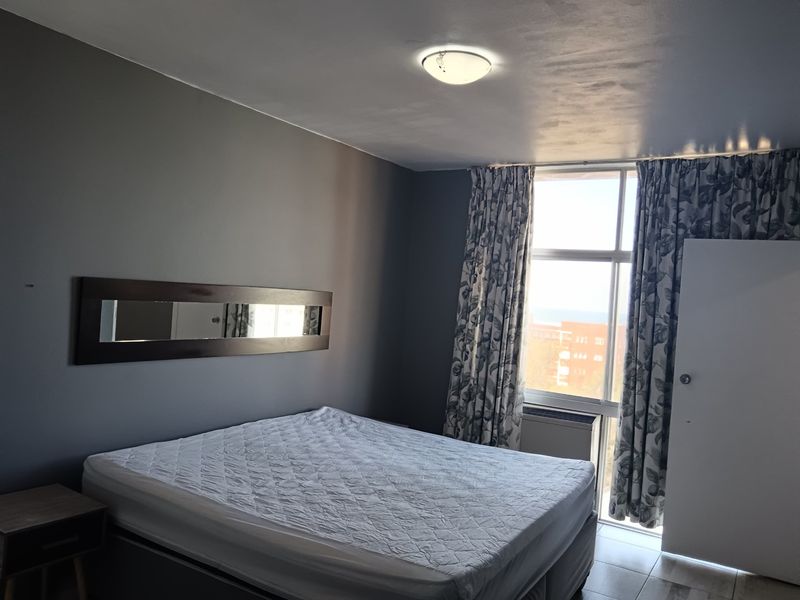 A bedroom featuring dark grey walls, a large window with natural light, and a ceiling light fixture.