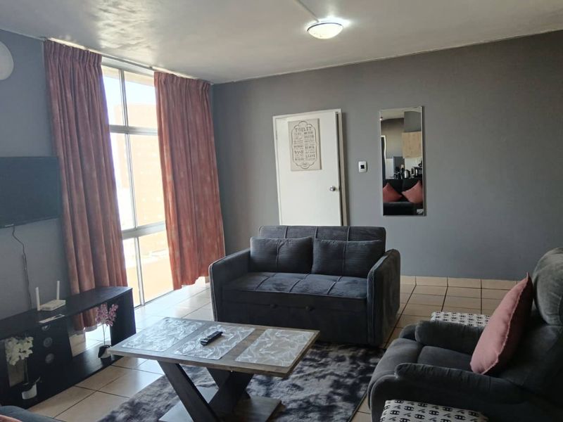 A living room featuring tiled flooring, a large window with curtains, and neutral grey wall paint.