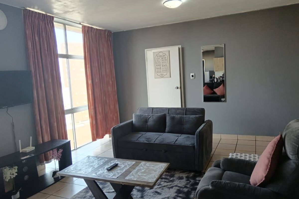 A living room featuring tiled flooring, a large window with curtains, and neutral grey wall paint.