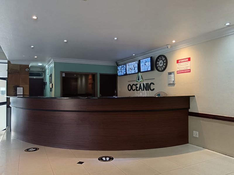 A professional apartment building reception area featuring a curved wooden front desk, tiled flooring, and integrated security monitoring systems.