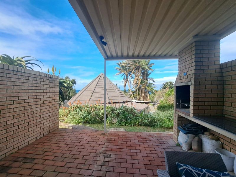 Covered outdoor patio featuring a built-in brick braai, brick paving, and views of the surrounding garden and landscape.