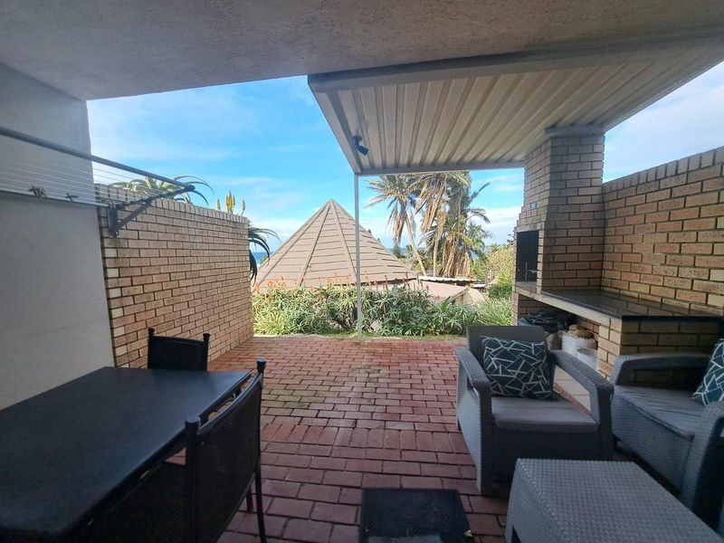 Covered patio area featuring brick paving and a built-in brick braai, offering an outdoor entertainment space with garden and partial sea views.