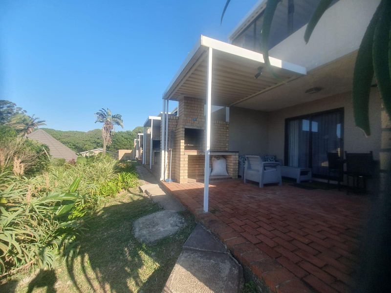 A covered outdoor patio featuring a built-in brick braai and red brick paving, providing direct access to the apartment through sliding glass doors.