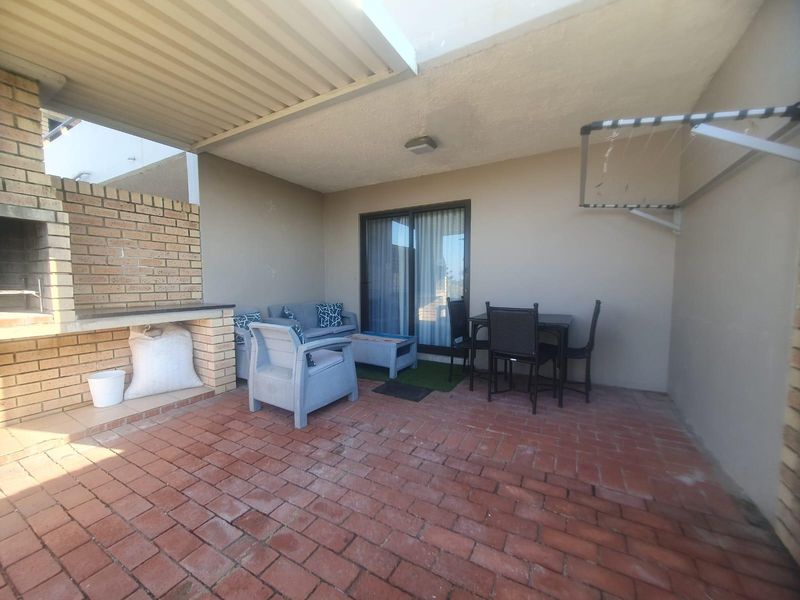Covered patio area featuring brick paving, a built-in brick braai, and direct access to the interior via sliding glass doors.