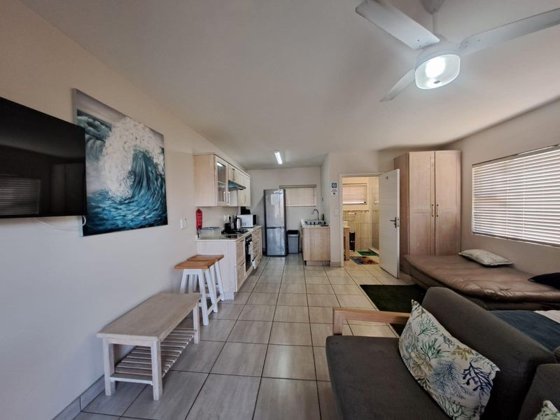 Open-plan living area featuring tiled flooring, a ceiling fan, and a functional kitchen with built-in cabinetry, oven, and hob, leading to an adjacent bathroom.