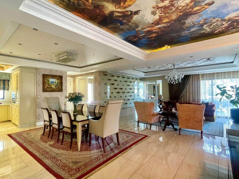Spacious open-plan living and dining area featuring high-end marble flooring, intricate coffered ceilings with artistic murals, and a sophisticated built-in wine display wall.