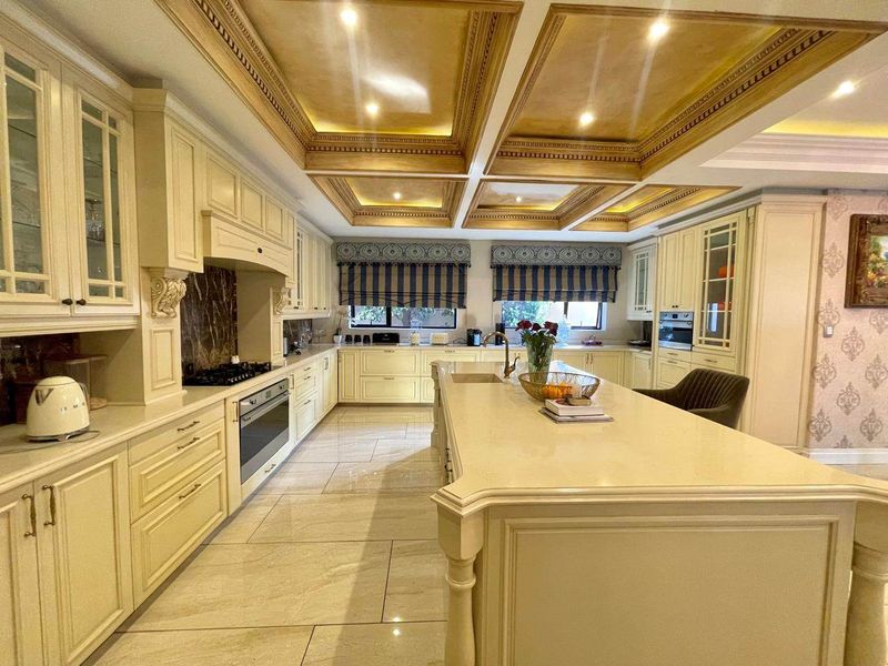 Spacious traditional kitchen featuring a large central island, stone countertops, custom cabinetry, and an elegant coffered ceiling with integrated lighting.
