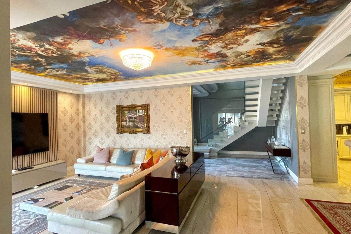 Luxurious living room featuring a dramatic painted ceiling mural, crystal chandelier, marble flooring, and a modern staircase with glass balustrades.