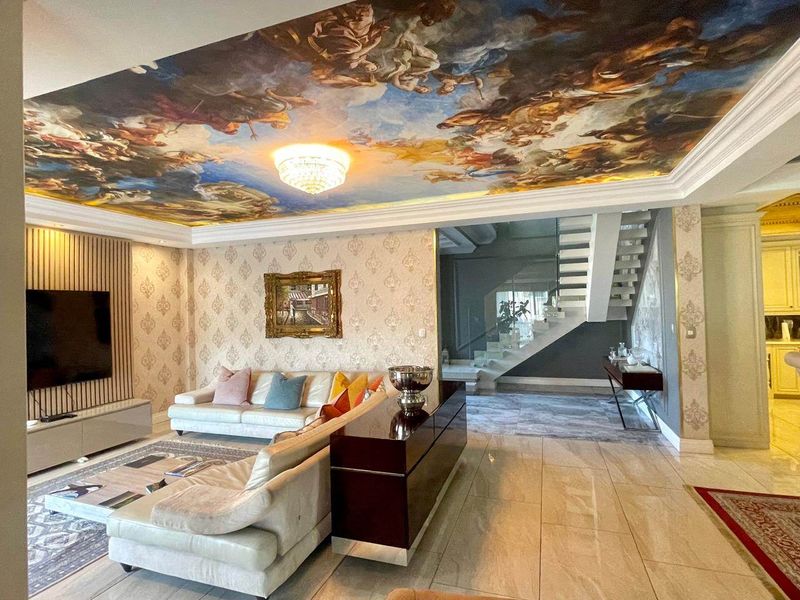 Luxurious living room featuring a dramatic painted ceiling mural, crystal chandelier, marble flooring, and a modern staircase with glass balustrades.