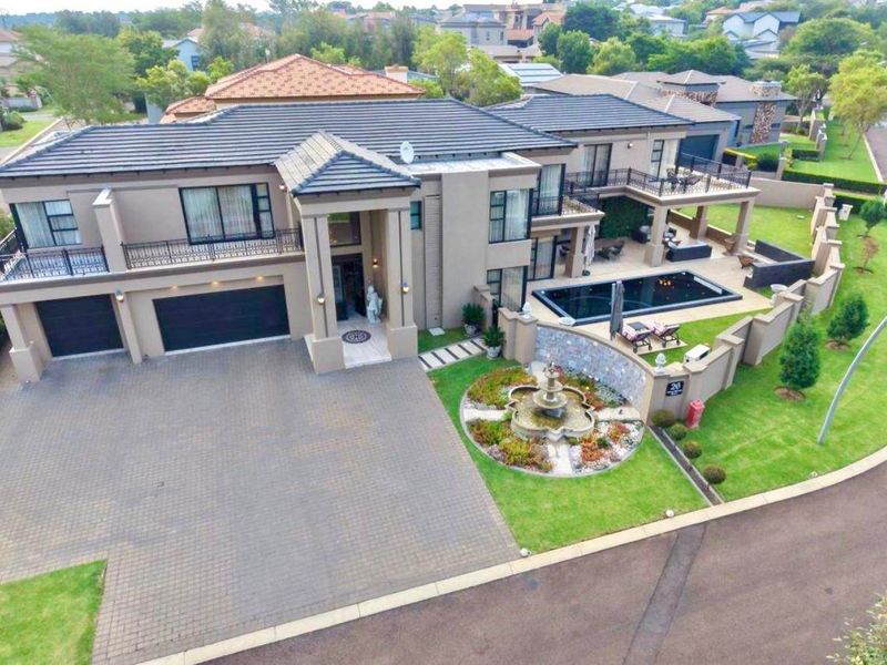 Aerial view of a modern luxury residence featuring a paved driveway, double garage, swimming pool, and a landscaped garden with a stone fountain.