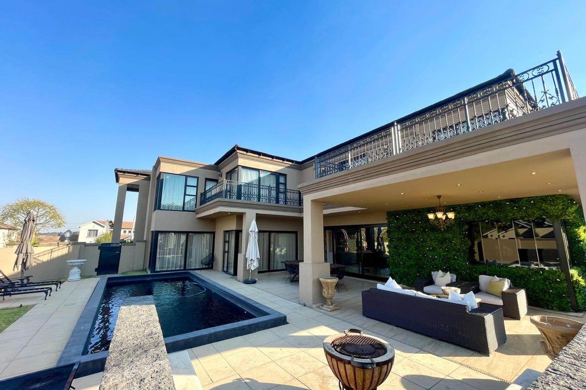 Spacious rear exterior featuring a modern swimming pool, covered patio area, and an upper-level balcony with decorative wrought iron railings.