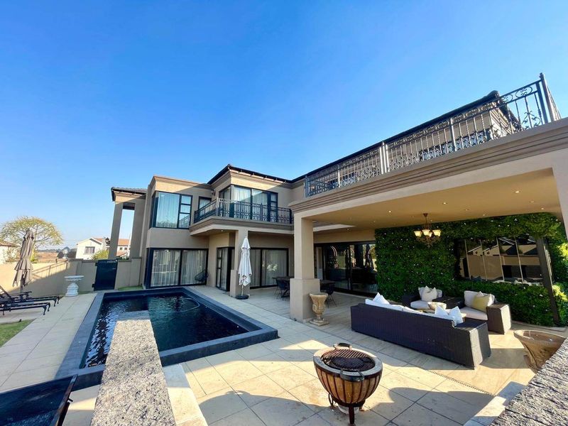 Spacious rear exterior featuring a modern swimming pool, covered patio area, and an upper-level balcony with decorative wrought iron railings.
