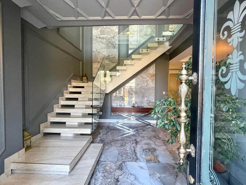 Grand entrance foyer featuring luxurious marble flooring, a striking floating staircase with glass balustrades, and elegant coffered ceilings with detailed wall molding.