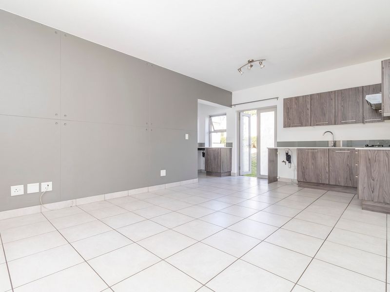 An open-plan living and kitchen area featuring tiled floors, modern wood-grain cabinetry, and direct access to an outdoor space through a glass door.