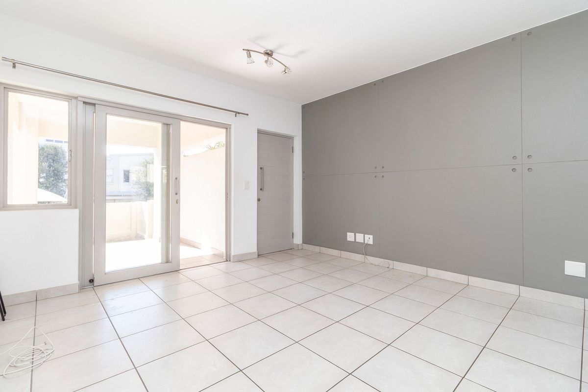 A bright, empty living area featuring neutral tiled flooring, a modern grey panelled feature wall, and sliding glass doors leading to an outdoor space.