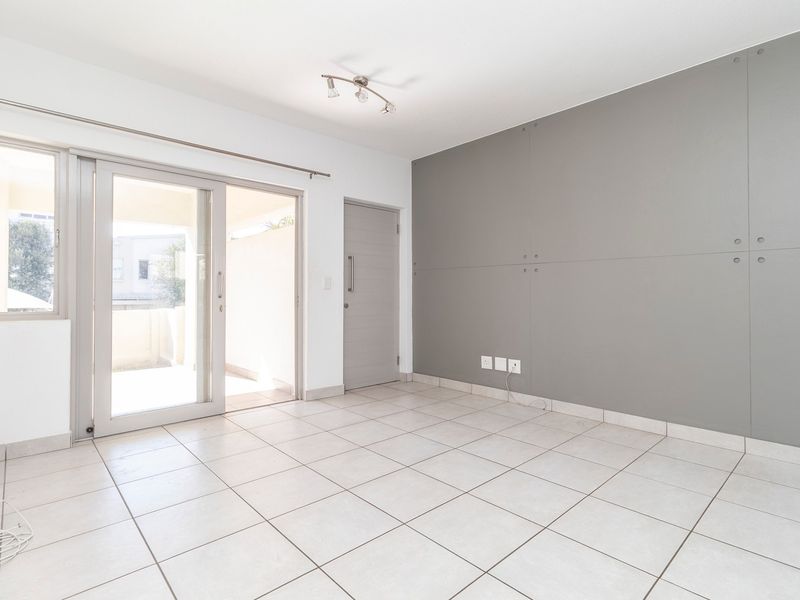 A bright, empty living area featuring neutral tiled flooring, a modern grey panelled feature wall, and sliding glass doors leading to an outdoor space.