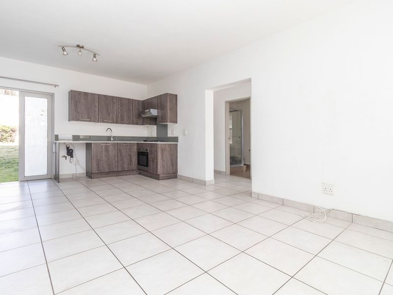 Open-plan living area featuring tiled floors, a compact kitchen with built-in cabinetry, and direct access to an outdoor garden space.