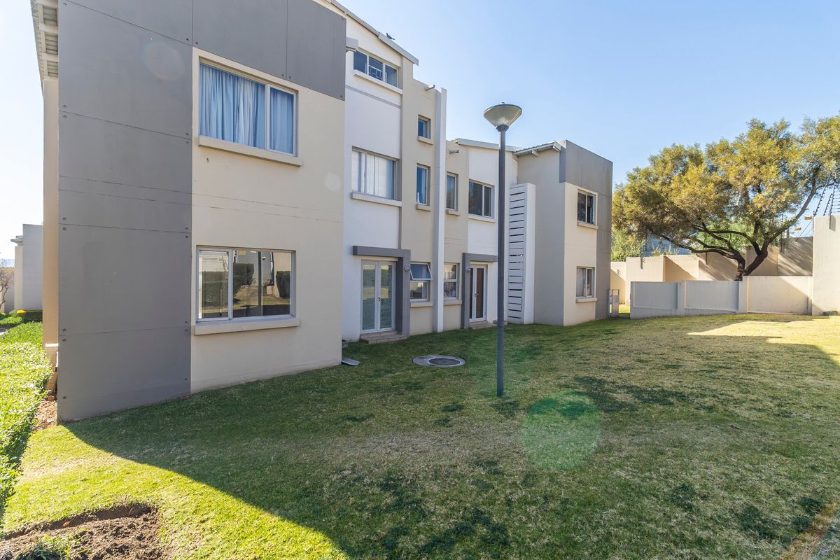 Rear view of a modern apartment complex featuring a well-maintained lawn, paved access points, and contemporary exterior facade finishes.