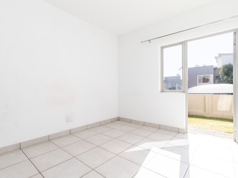 A bright, empty bedroom featuring neutral tiled flooring and a sliding door providing direct access to an outdoor area.