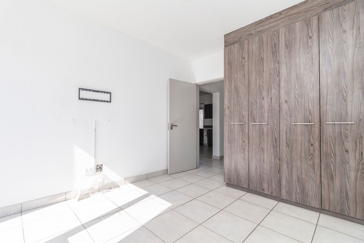 A bright, empty bedroom featuring neutral tiled flooring and modern wood-grain built-in cupboards, offering a clean and versatile living space.
