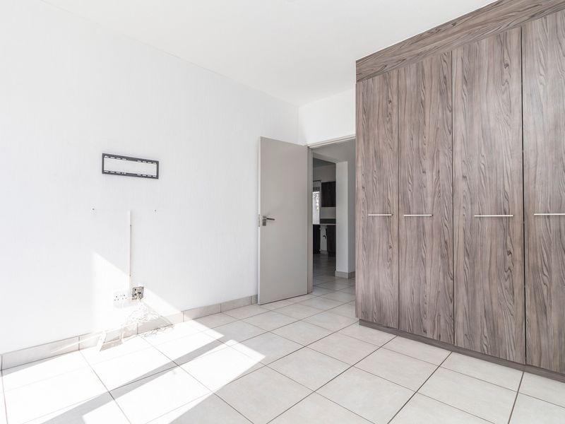 A bright, empty bedroom featuring neutral tiled flooring and modern wood-grain built-in cupboards, offering a clean and versatile living space.