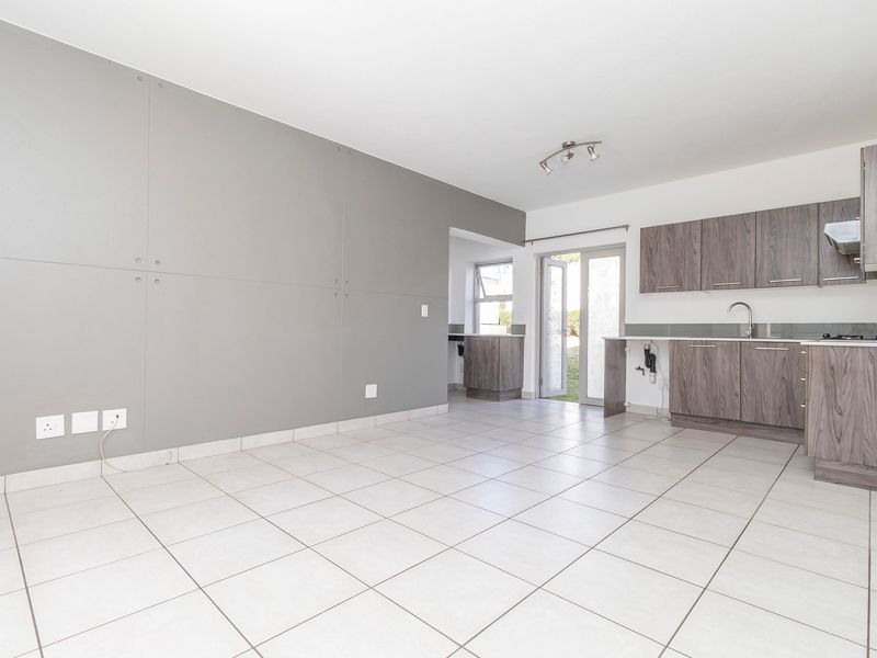An open-plan living and kitchen area featuring tiled flooring, modern wood-finish cabinetry, and direct access to an outdoor space through a glass sliding door.