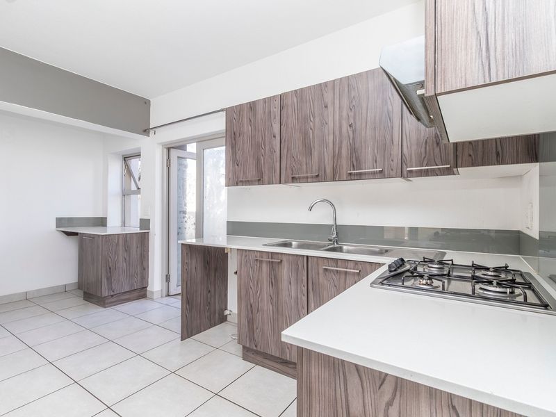 Modern kitchen featuring wood-grain cabinetry, a gas hob with extractor fan, stainless steel sink, and tiled flooring with direct access to the exterior.
