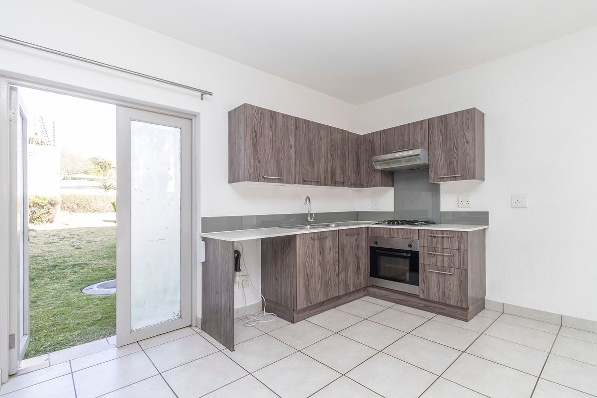 A clean, modern kitchen featuring wood-grain cabinetry, built-in oven and hob, tiled floors, and direct access to the garden through a glass sliding door.