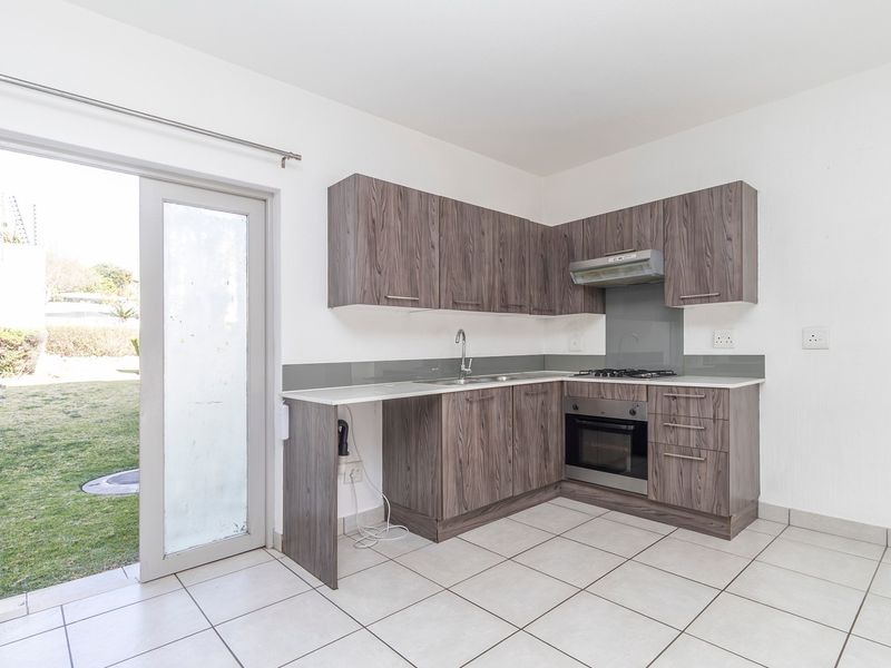 A clean, modern kitchen featuring wood-grain cabinetry, built-in oven and hob, tiled floors, and direct access to the garden through a glass sliding door.