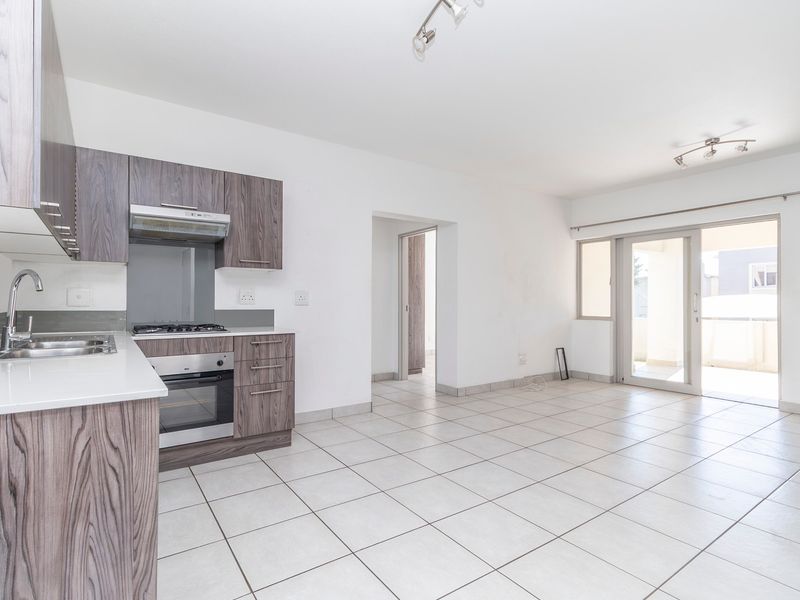 Bright open-plan kitchen and living area featuring modern wood-finish cabinetry, built-in appliances, tiled flooring, and direct access to a private balcony.
