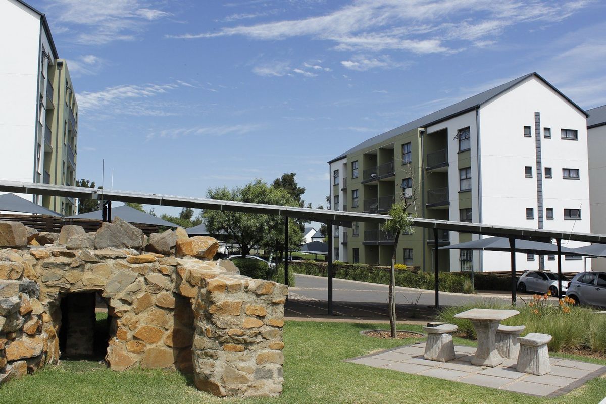 Exterior view of an apartment complex featuring a landscaped garden, stone feature, and covered walkways connecting the residential buildings.