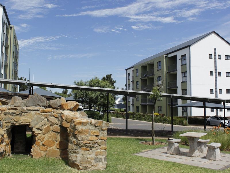 Exterior view of an apartment complex featuring a landscaped garden, stone feature, and covered walkways connecting the residential buildings.