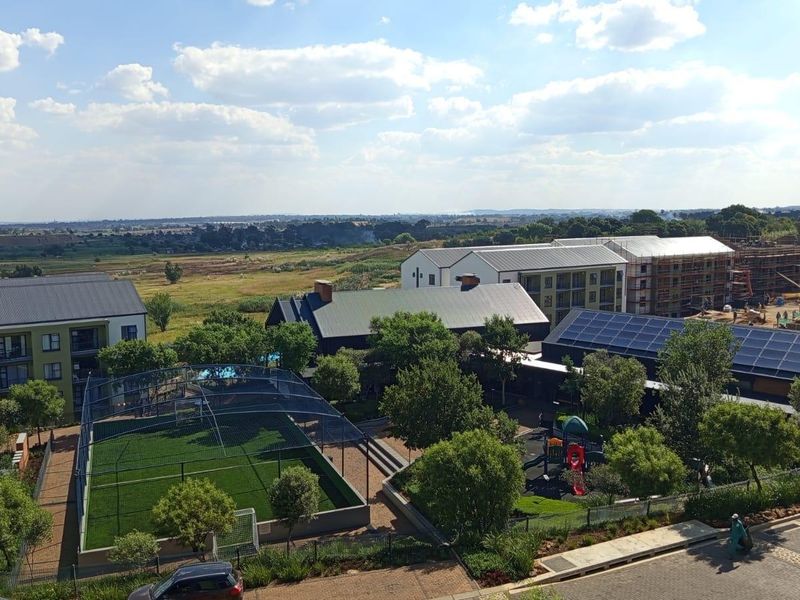 An elevated aerial view of the apartment complex grounds, featuring a sports court, playground, and buildings with solar panel installations.