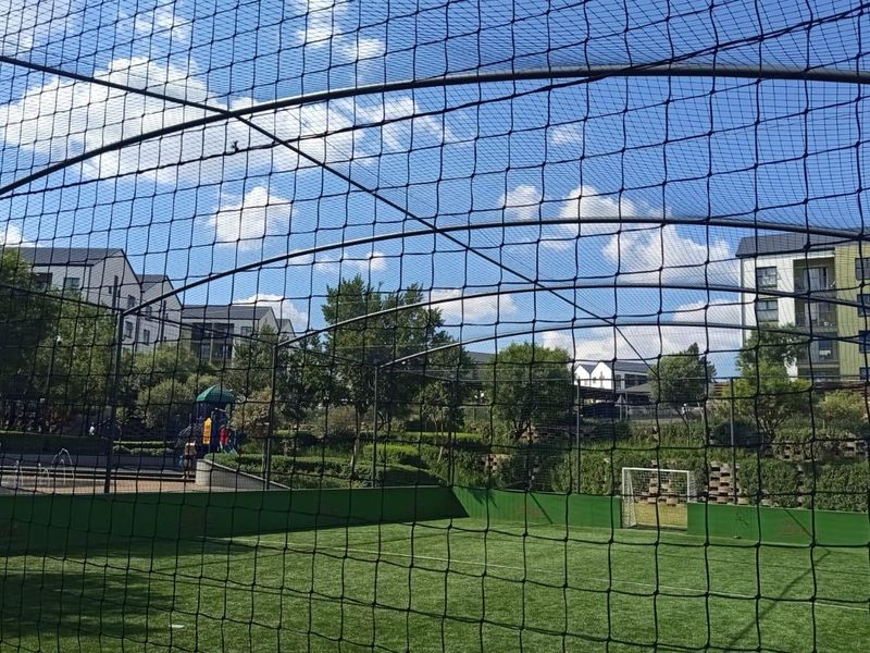 A well-maintained outdoor sports facility featuring artificial turf, perimeter netting, and a goal post within a residential apartment complex.
