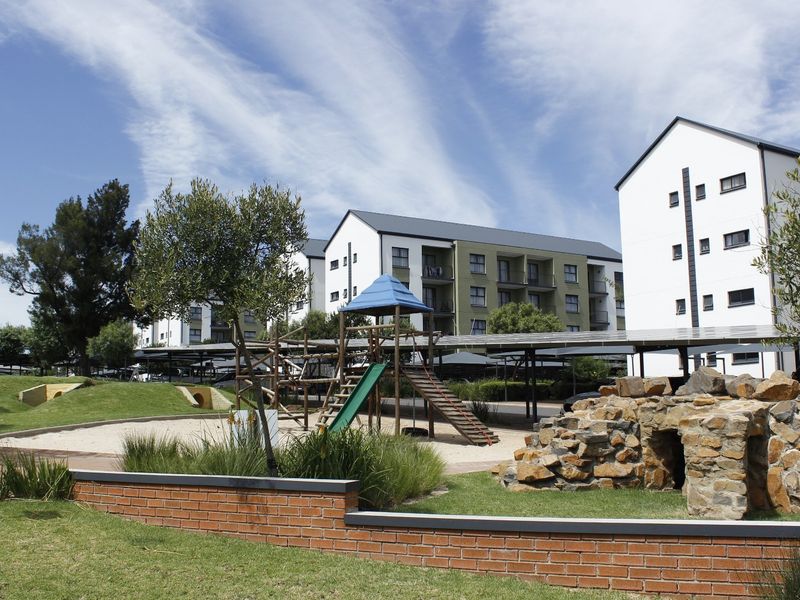 Communal garden area featuring a playground, stone landscaping, and covered solar carports within a well-maintained apartment complex.