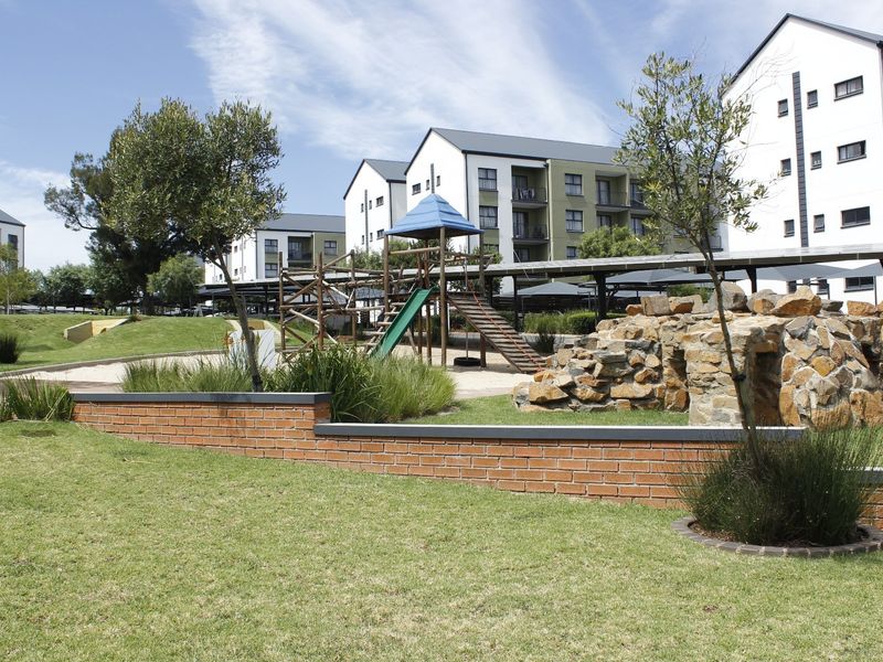 Well-maintained communal garden area featuring a brick retaining wall, stone landscaping, and a children's playground set within an apartment complex.