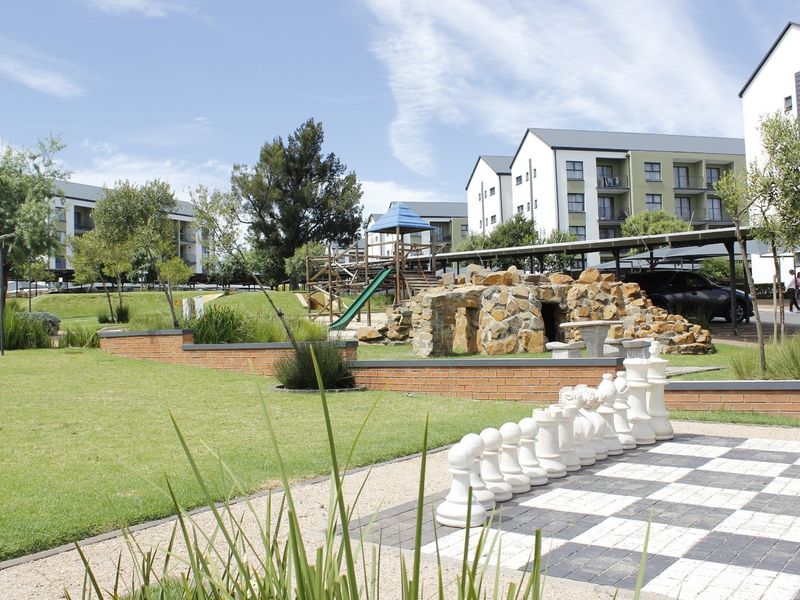 Well-maintained communal garden area featuring landscaped lawns, brick retaining walls, a stone feature, and outdoor recreational facilities within an apartment complex.
