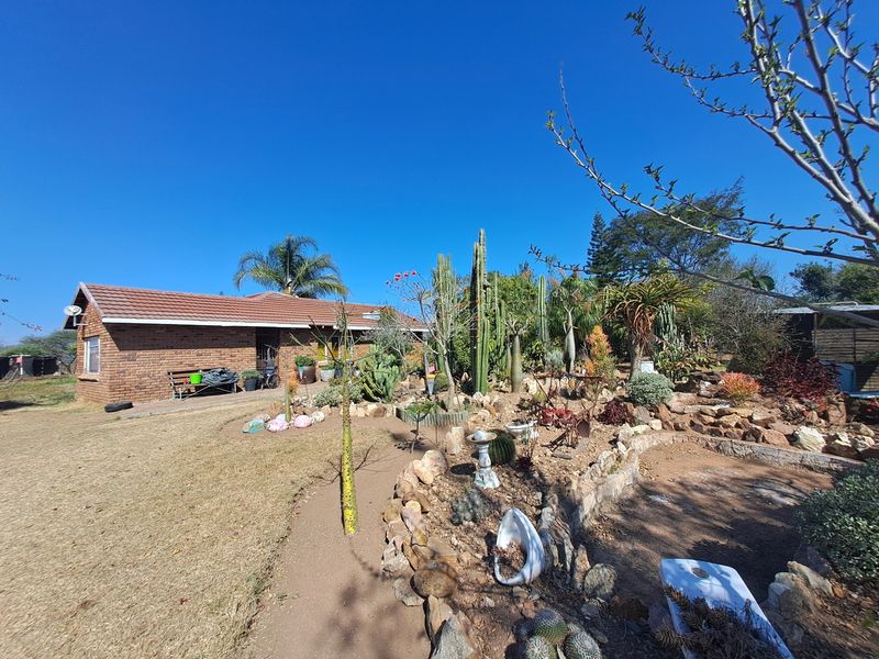 A landscaped garden featuring a stone retaining wall, diverse cacti, and a brick farmhouse exterior with a tiled roof.