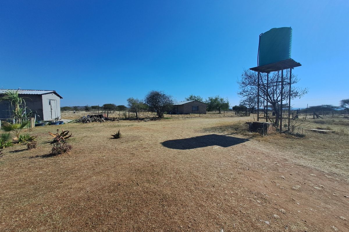 A wide view of the farm grounds featuring a raised water tank on a metal stand and a small outbuilding in the distance.